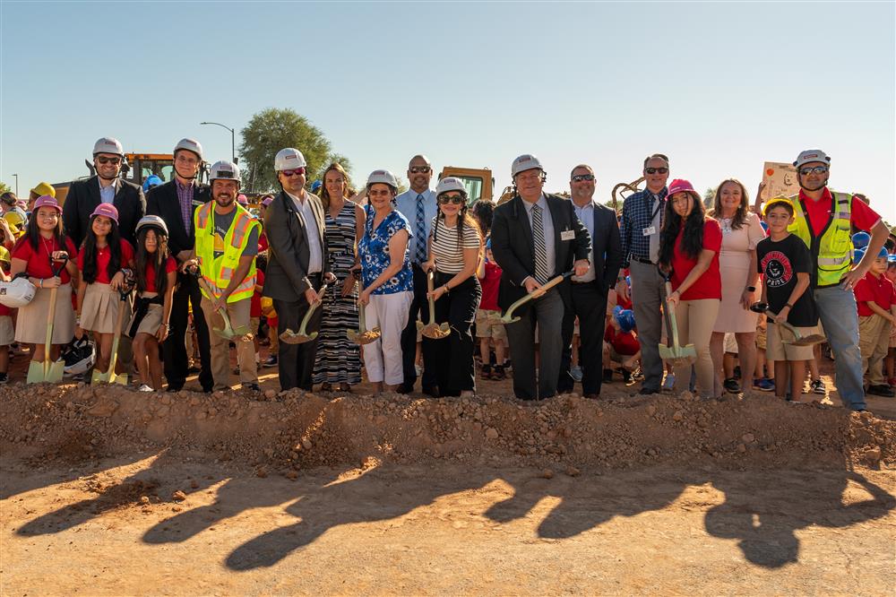 People dressed in hard hats and safety vests use shovels to dig into the ground